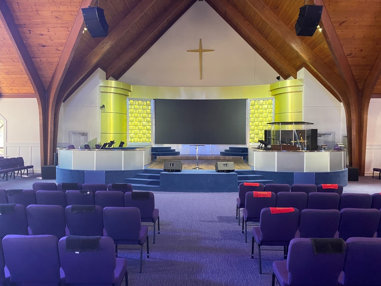 Modern sanctuary with purple carpet, wood ceiling, and yellow-lit cross